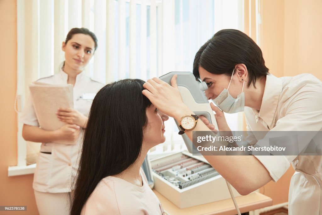 Nurse looking at optometrist examining female patient at hospital