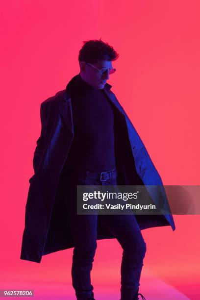 young male fashion model wearing leather overcoat standing against coral background - pindyurin foto e immagini stock