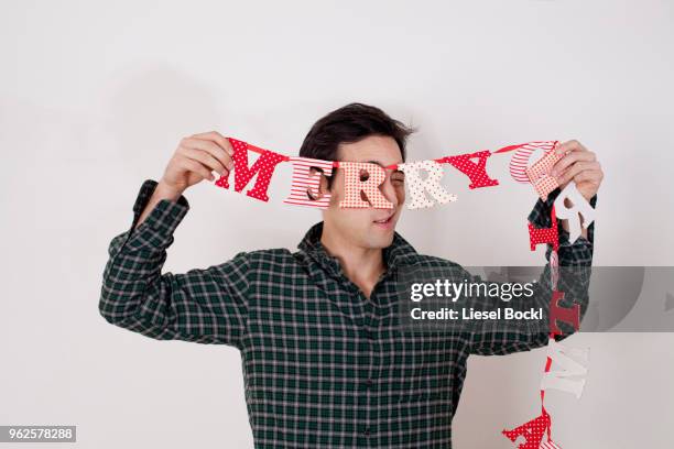 playful man holding merry christmas bunting while standing against white background - bunting white background fotografías e imágenes de stock