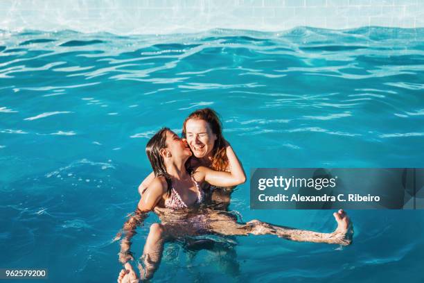high angle view of girl kissing happy mother in swimming pool - alexandra summers stockfoto's en -beelden