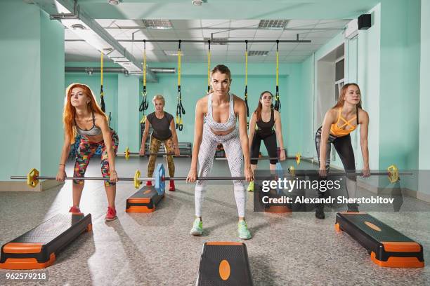 full length of trainer with determined women lifting barbell during step aerobics - sherstobitov stock pictures, royalty-free photos & images