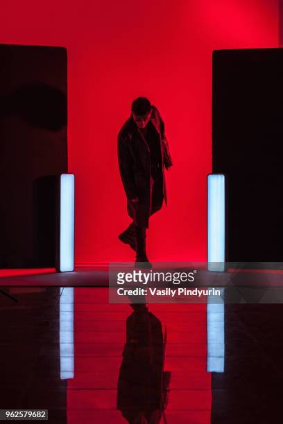 full length of young man standing amidst illuminated lights with reflection on floor in red studio - pindyurin stock-fotos und bilder