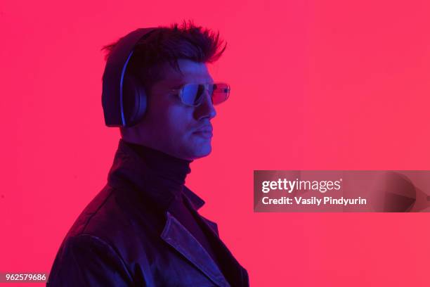 young male fashion model wearing headphones and sunglasses against coral background - pindyurin stock-fotos und bilder