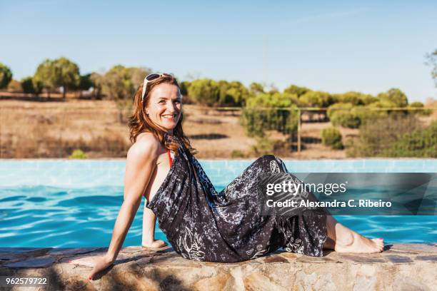 side view portrait of smiling mid adult woman wearing sarong sitting at poolside on sunny day - sarong stock pictures, royalty-free photos & images