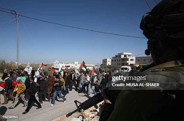 Israeli soldiers stand guard as protestors walk with flags during a demonstration against Israel's controversial separation barrier in the village of...