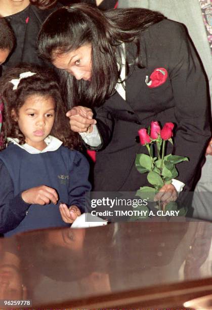 Jeanne Ashe, wife of the late Arthur Ashe, points out to daughter Camera as the casket of Ashe is lowered into the ground 10 February 1993 during...