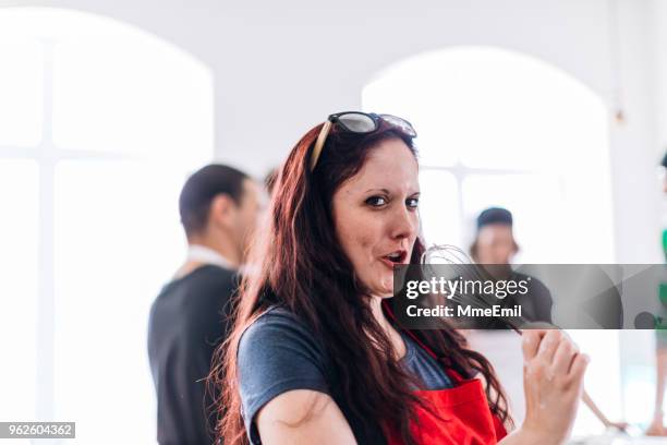 カメラを見て、料理ワーク ショップ コミュニティ センターでワイヤー泡立て器で歌う若い女性 - wire whisk ストックフォトと画像