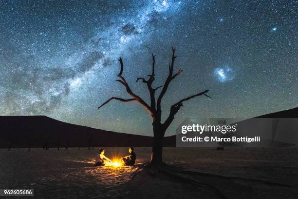 two people sheltering at night under a dead acacia tree in deadvlei - camp site stock-fotos und bilder