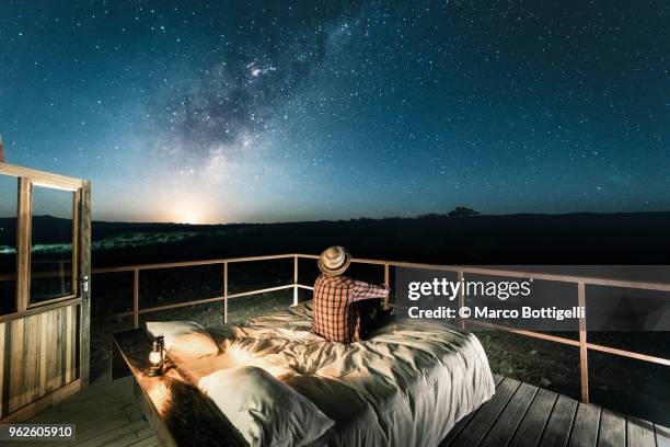 tourist sitting in bed outdoors under a starry sky - astronomia foto e immagini stock