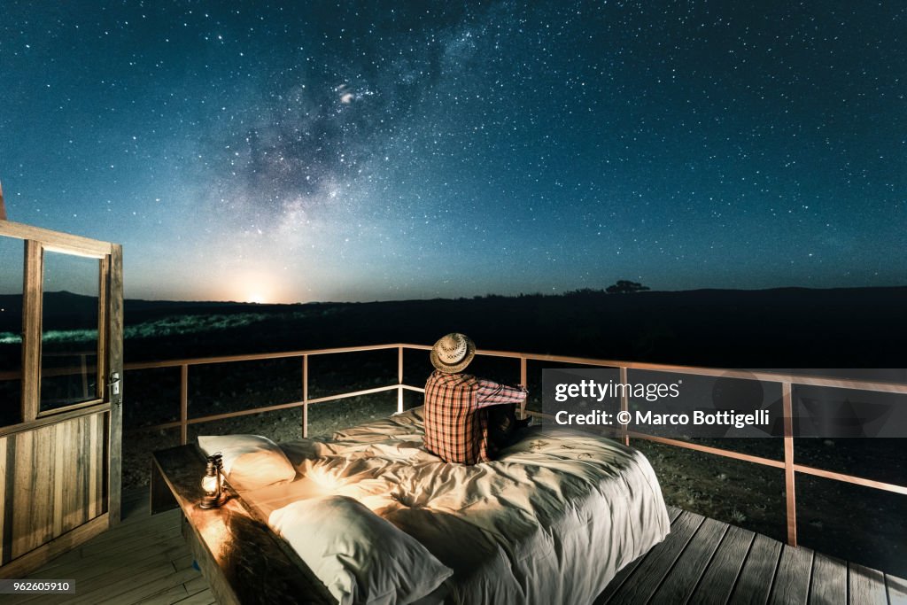 Tourist sitting in bed outdoors under a starry sky