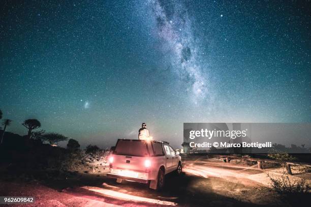 man sitting on a 4x4 car roof under the milky way - car roof stock pictures, royalty-free photos & images