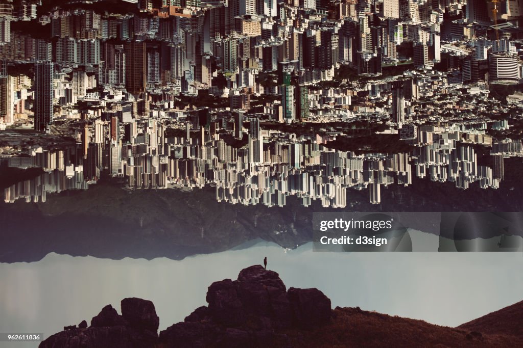 Silhouette of man standing on top of mountain with urban cityscape turning up side down