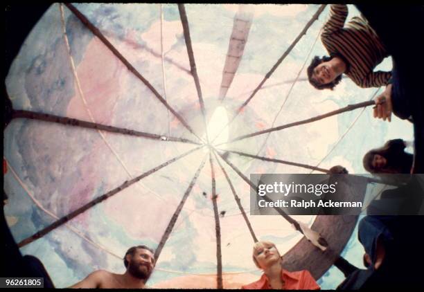 Fish-eye view looking up several smiling festival goers and at the clouds painted on a tipi during the Woodstock Music and Arts Fair, Bethel, New...