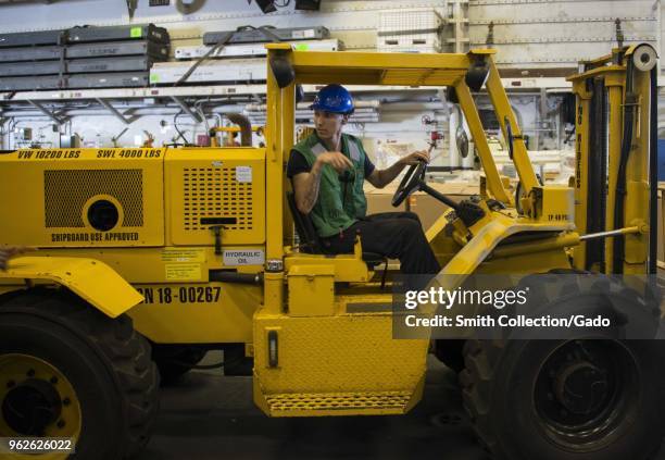 Photograph of logistics specialist 3rd Class Edgar Reyes driving a forklift in the hangar bay of the USS Iwo Jima assault ship, May 15, 2018.