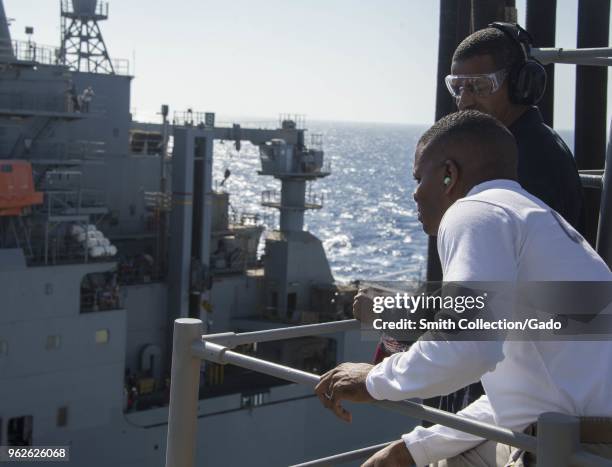 Photograph of Command Master Chief Ervin H Byrd III and another soldier watching the dry cargo and ammunition ship USNS Amelia Earhart conduct a...
