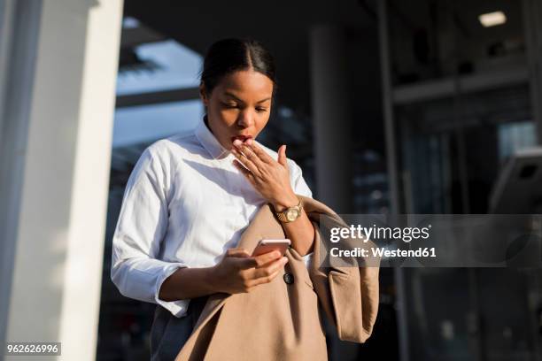 portrait of shocked businesswoman reading email on her mobile phone - mão na boca imagens e fotografias de stock