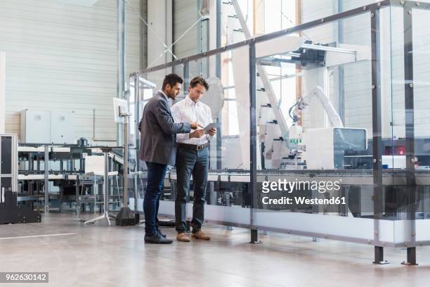 two businessmen with tablet talking in modern factory - herstellendes gewerbe stock-fotos und bilder