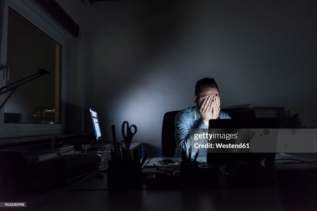 Exhausted businessman sitting at desk in office at night