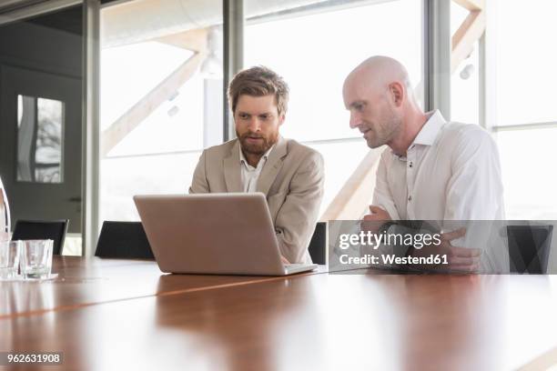 two businessmen sharing laptop in conference room - consulting laptop manager stock-fotos und bilder