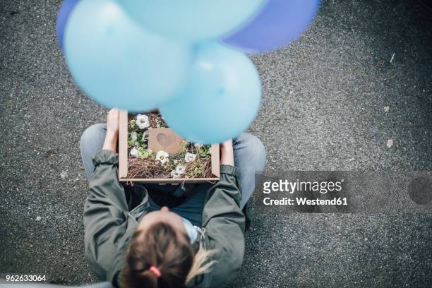 woman with present in cardboard box and blue balloons sitting on the ground - luxury lounges stock pictures, royalty-free photos & images