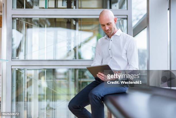 smiling businessman sitting at the window using tablet - schweiz business stock-fotos und bilder