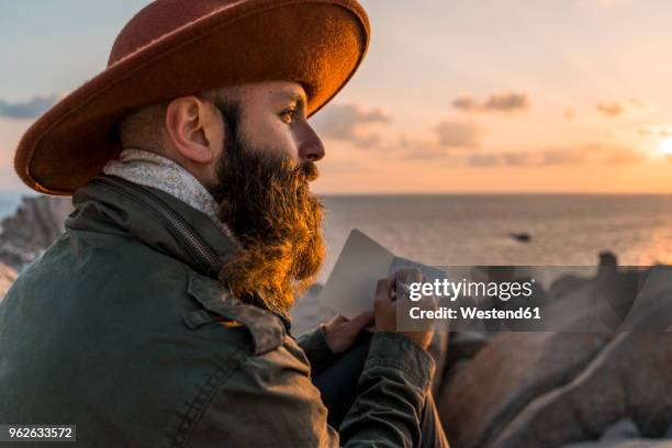 italy, sardinia, bearded man with notebook in front of the sea at sunset - travel writer stock pictures, royalty-free photos & images