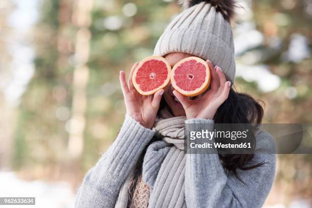 laughing young woman wearing knitwear covering her eyes with halves of grapefruit - grapefruit bildbanksfoton och bilder