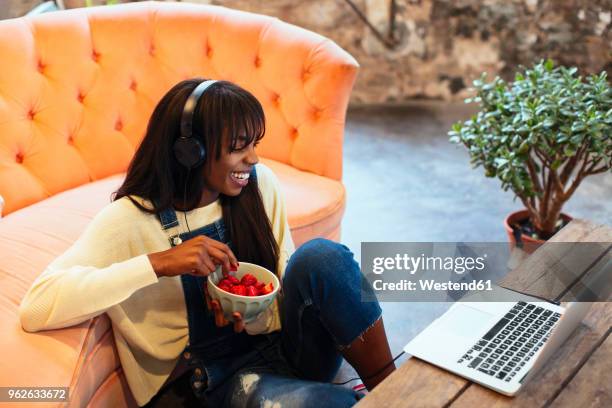 laughing young woman sitting on the floor of her loft using laptop and headphones - jeans latzhose frau stock-fotos und bilder