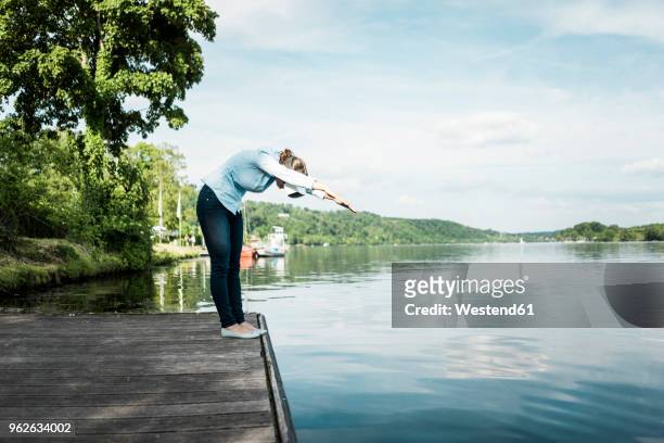 woman on jetty wearing vr glasses pretending to dive into a lake - down blouse stockfoto's en -beelden