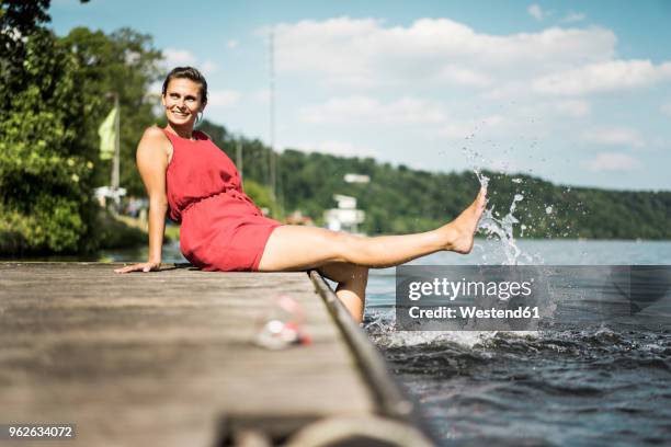 happy woman sitting on jetty at a lake - white women feet fotografías e imágenes de stock