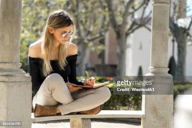 young woman with notebook sitting on bench writing down something - left handed stock pictures, royalty-free photos & images