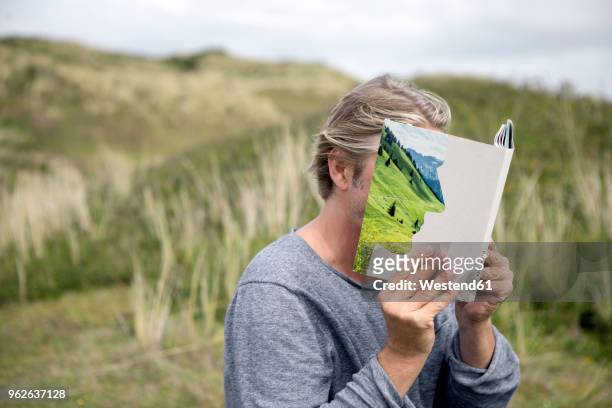 man reading story book in the dunes, covering his face - literature fotografías e imágenes de stock