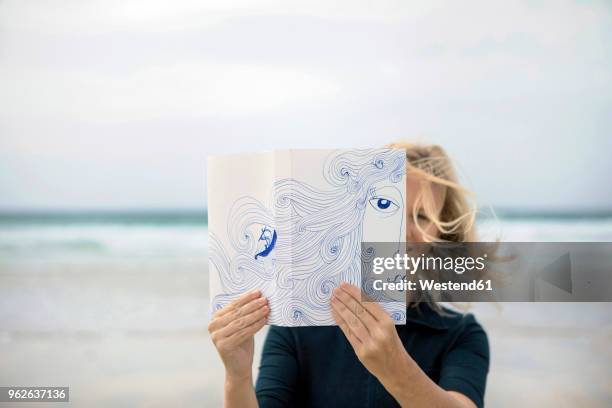 woman covering face with book, reading poetry on beach - schizophren stock-fotos und bilder