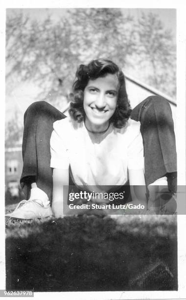 Black and white photograph, showing a smiling, dark-haired woman, outdoors, wearing a light colored top, seemingly contorted into a frog-like pose by...