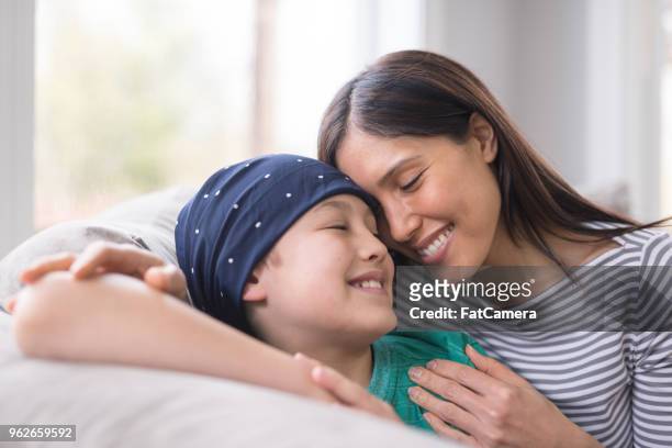 un niño de primaria edad luchando contra el cáncer se encuentra con su madre en el sofá - cancer infantil fotografías e imágenes de stock