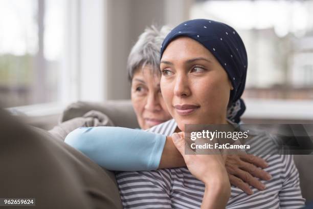 an asian woman in her 60s embraces her mid-30s daughter who is battling cancer - family support stock pictures, royalty-free photos & images