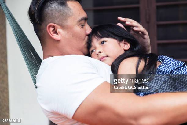 father embracing his daughter and kissing on the forehead on the hammock - hammock asia stock pictures, royalty-free photos & images