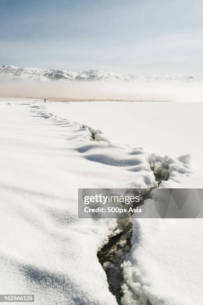 crack in ice and snowcapped mountains in background, xinjiang uygur autonomous region, china - ice crack stock-fotos und bilder