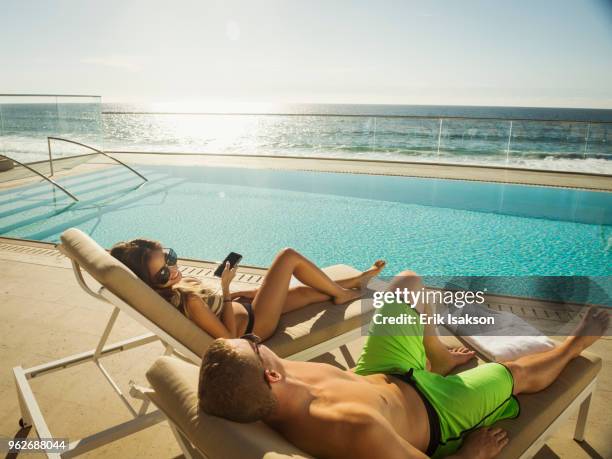 couple relaxing by swimming pool by ocean - sunbed stock-fotos und bilder