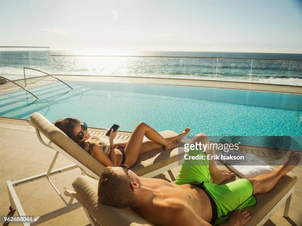 couple relaxing by swimming pool by ocean - sun lounger 個照片及圖片檔