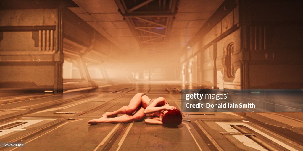 Woman lies curled up on floor of futuristic corridor