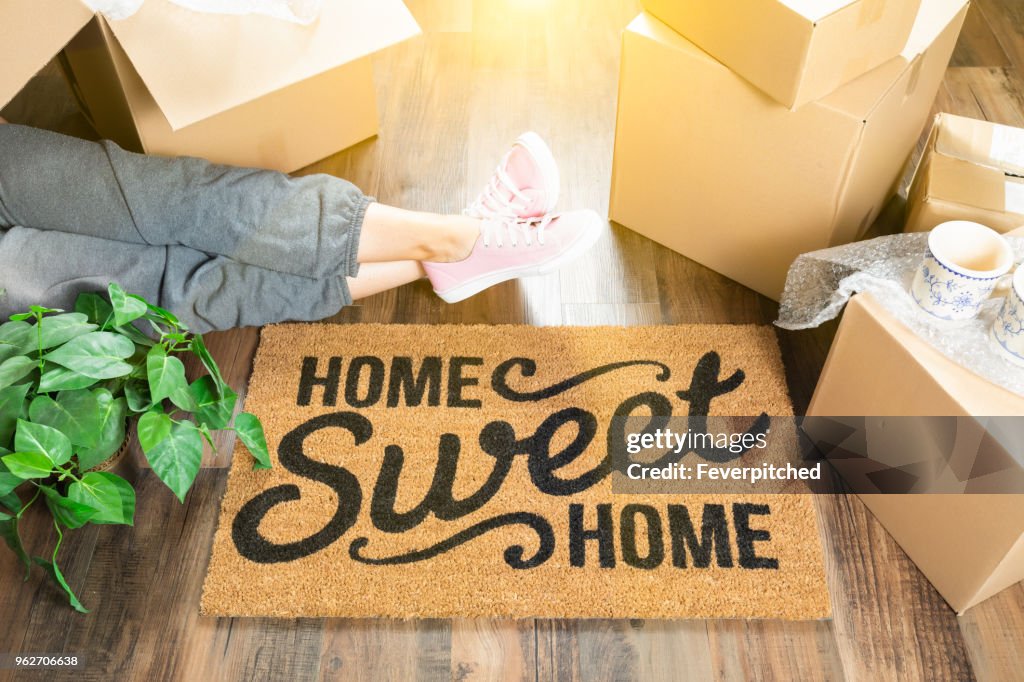 Woman Wearing Sweats Relaxing Near Home Sweet Home Welcome Mat, Moving Boxes and Plant.