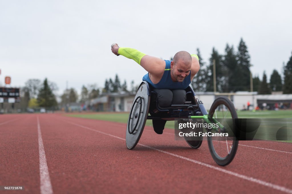 Adaptive Athlet training auf seinem Rollstuhl Racing auf einer Stadion-Strecke