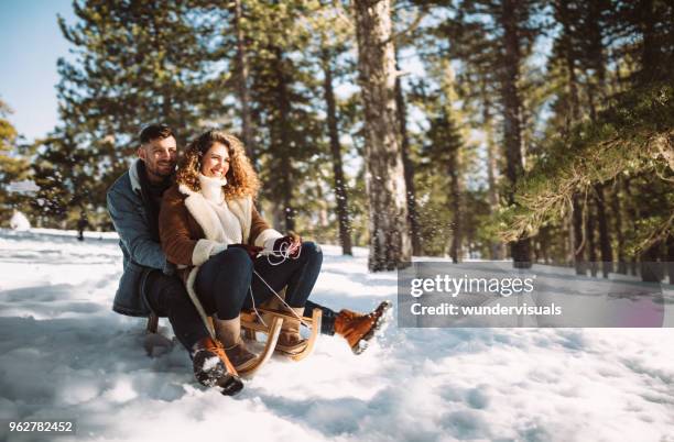 young couple on christmas holidays riding sledge in the snow - sleigh stock pictures, royalty-free photos & images
