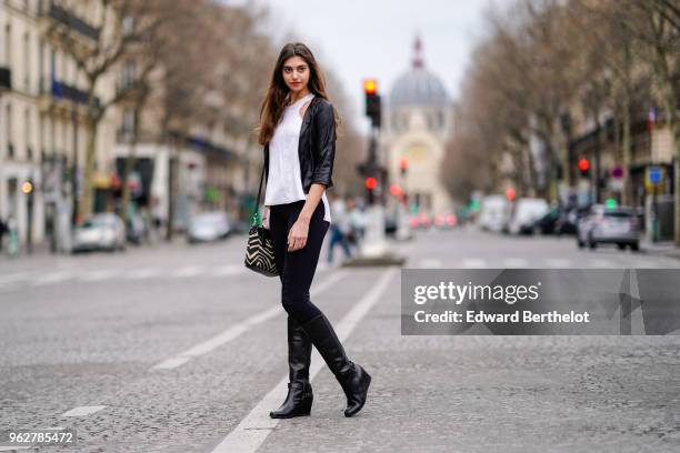 Amanda Derhy wears a white sleeveless tank top, black pants, a black leather jacket, a bag, black leather boots, on April 2, 2018 in Paris, France.