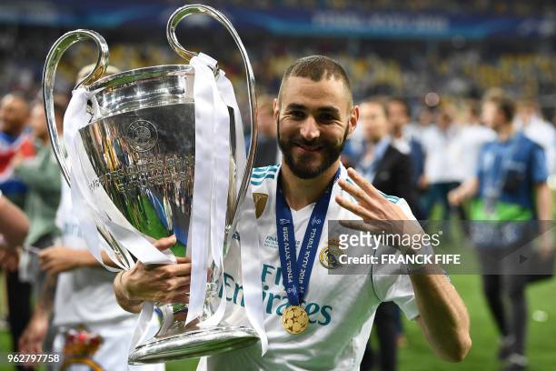Real Madrid's French forward Karim Benzema gestures the number four as he poses with the trophy after winning the UEFA Champions League final...