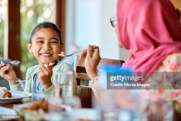 grandmother feeding food to smiling girl at home - islam family stock pictures, royalty-free photos & images