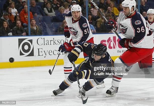 Andy McDonald of the St. Louis Blues passes the puck as Fedor Tyutin and Mathieu Roy of the Columbus Blue Jackets come on to defend on January 30,...