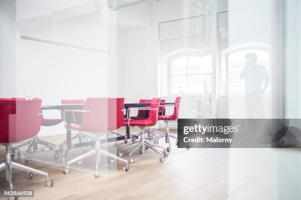 silhouette of a businessman using a mobile phone in a conference room of an office building. view through glass - münchen immobilie büro stock-fotos und bilder