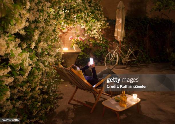 woman relaxing on deck chair in backyard at night, holding mobile phone - kathrin ziegler stockfoto's en -beelden